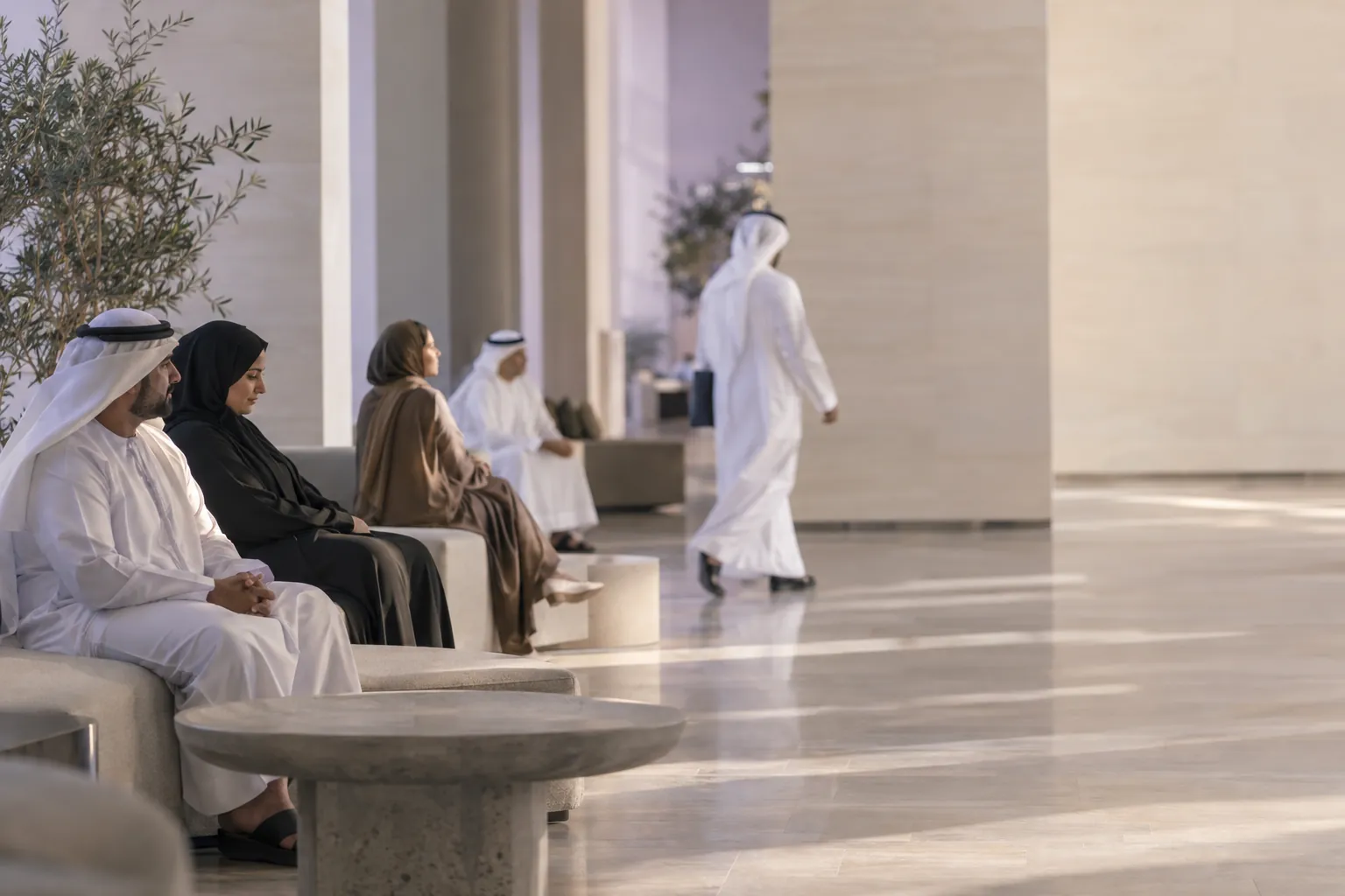 A calm modern public service hall in the Gulf with citizens waiting and a staff member walking past