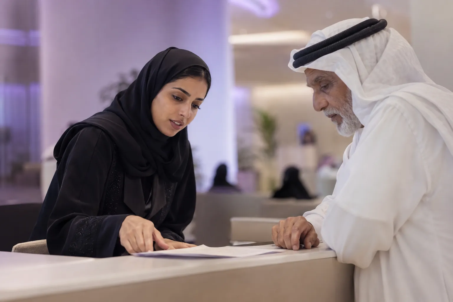 موظفة خدمة تساعد رجلاً مسناً عند مكتب في مركز خدمة عامة حديث في قطر