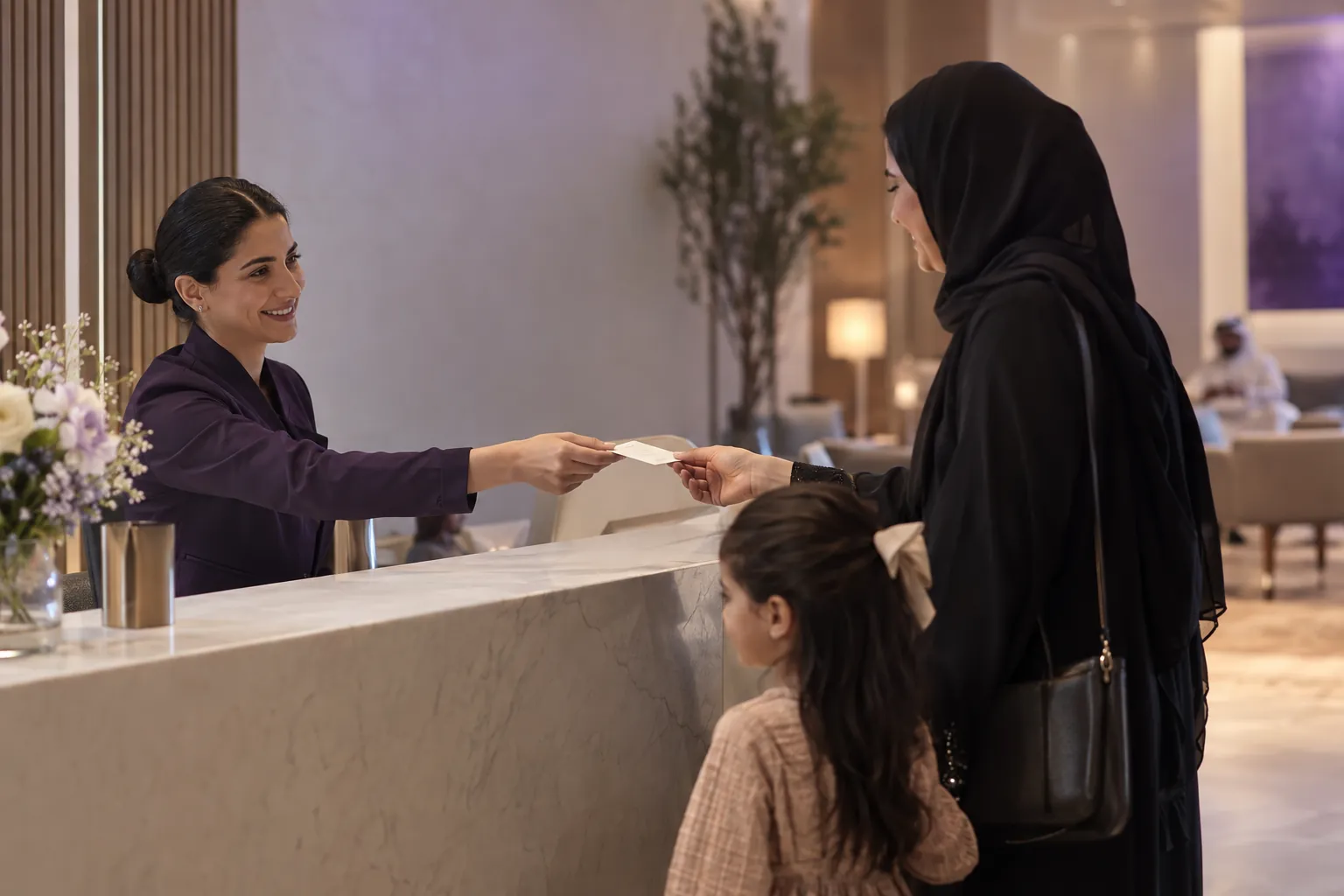 Receptionist in a Gulf clinic handing a card to a young mother with her child at the reception desk